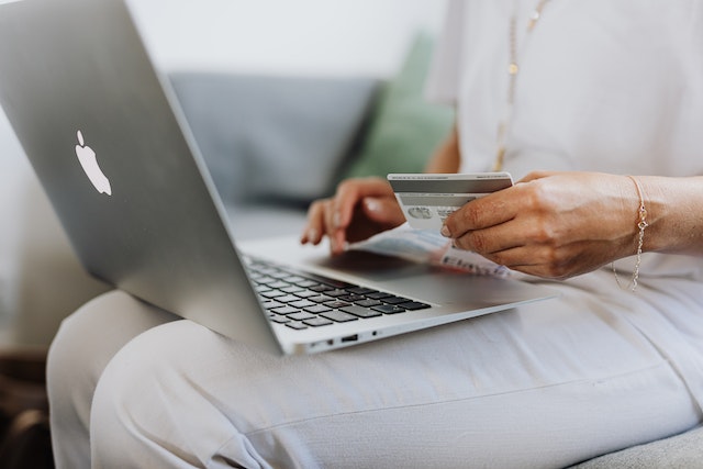 person holding a credit card while looking at their laptop to make an online payment